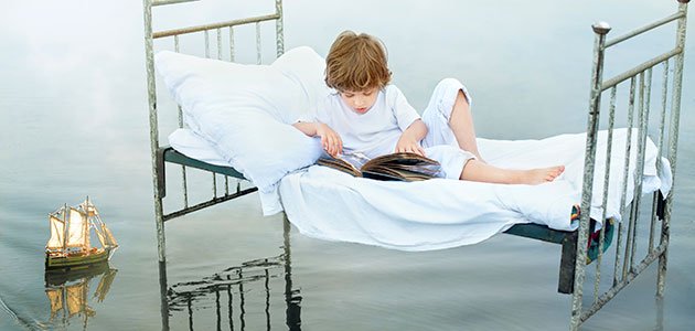 Niño lee en cama sobre el mar